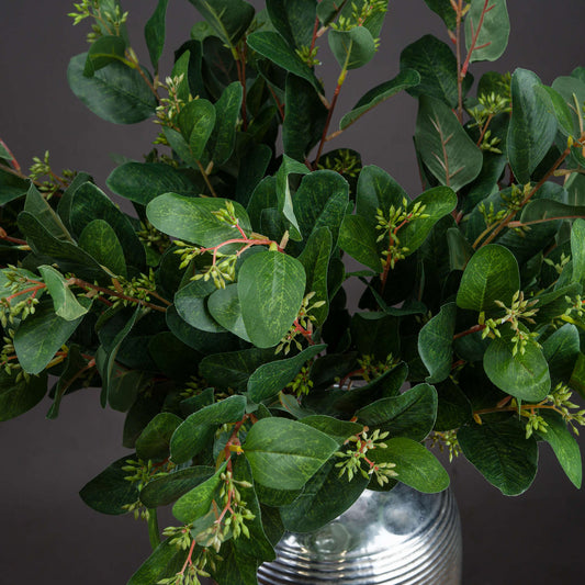 Green leaves in a silver vase against a dark background