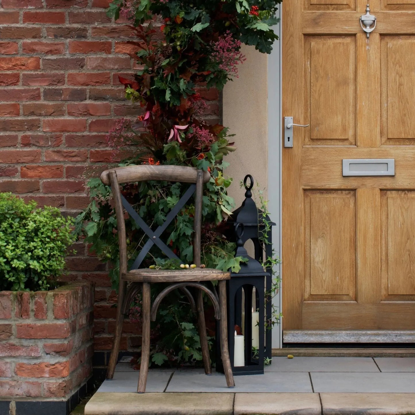 Wooden chair and decorative lantern on a porch with a wooden door and plants.