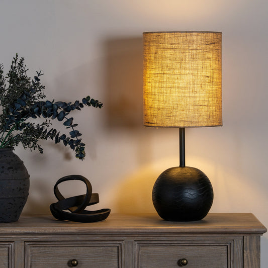 Table lamp with a textured shade on a wooden surface next to decorative items.