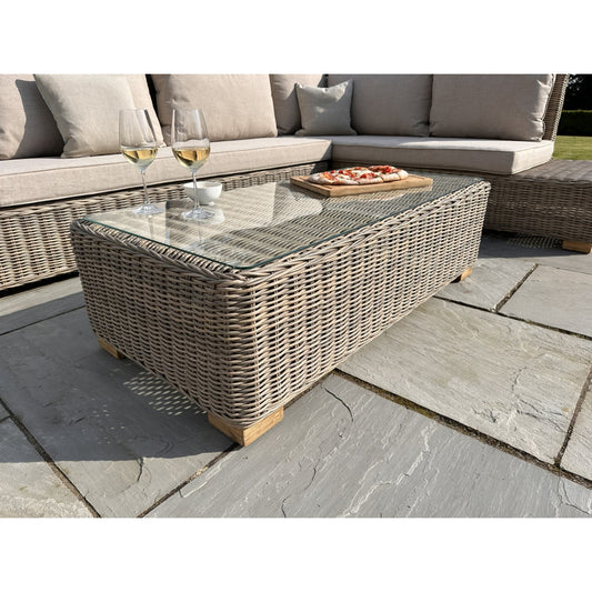 Wicker coffee table with a glass top on a patio with a sofa and glasses in the background.