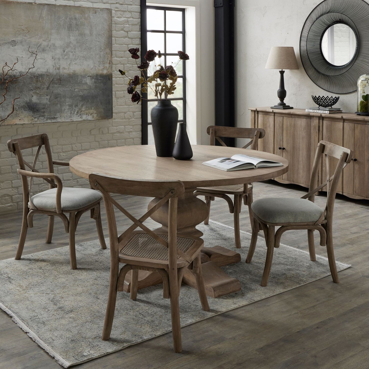 Dining room with wooden table and chairs on a rug, featuring a vase and book.