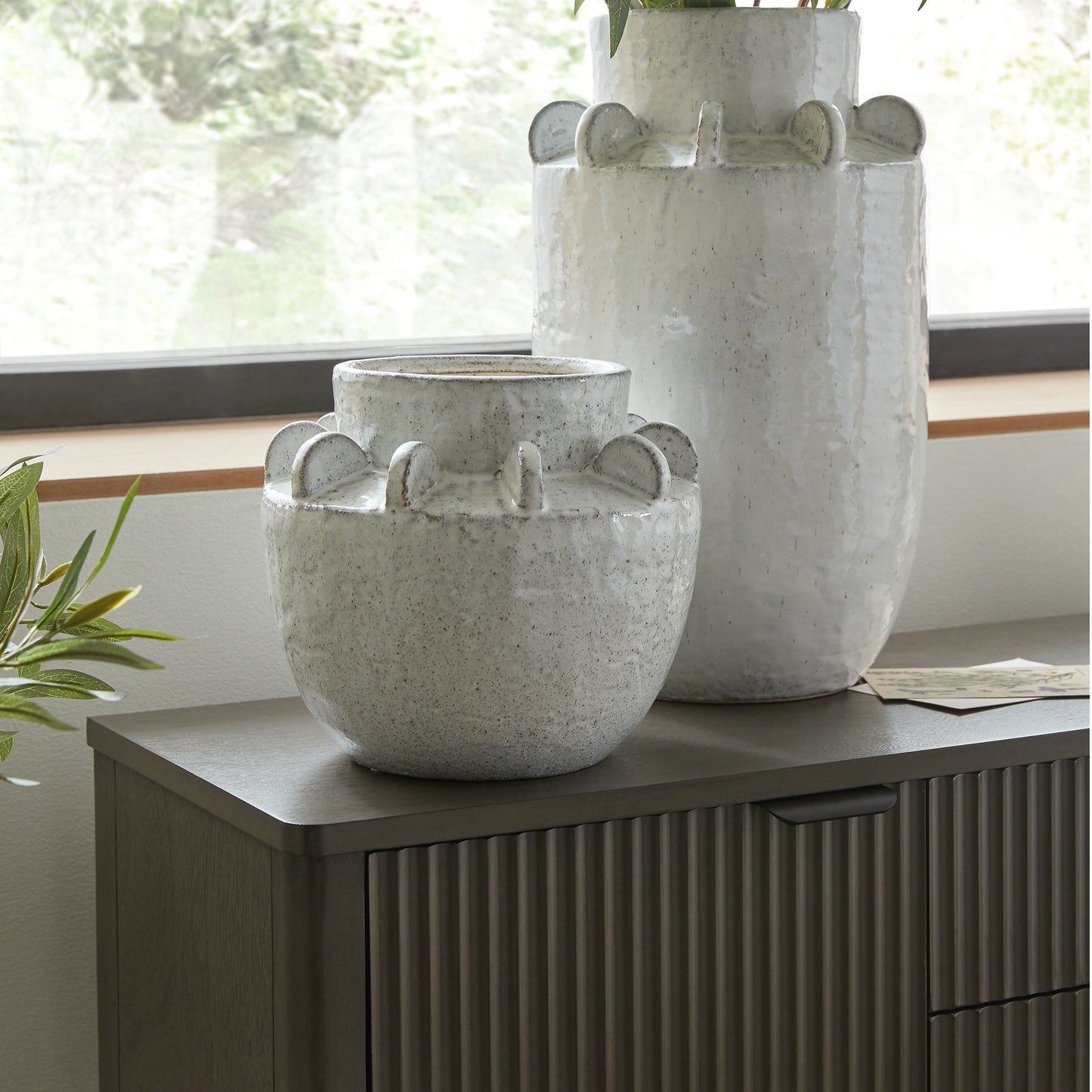 Two gray ceramic planters on a wooden surface with a window in the background