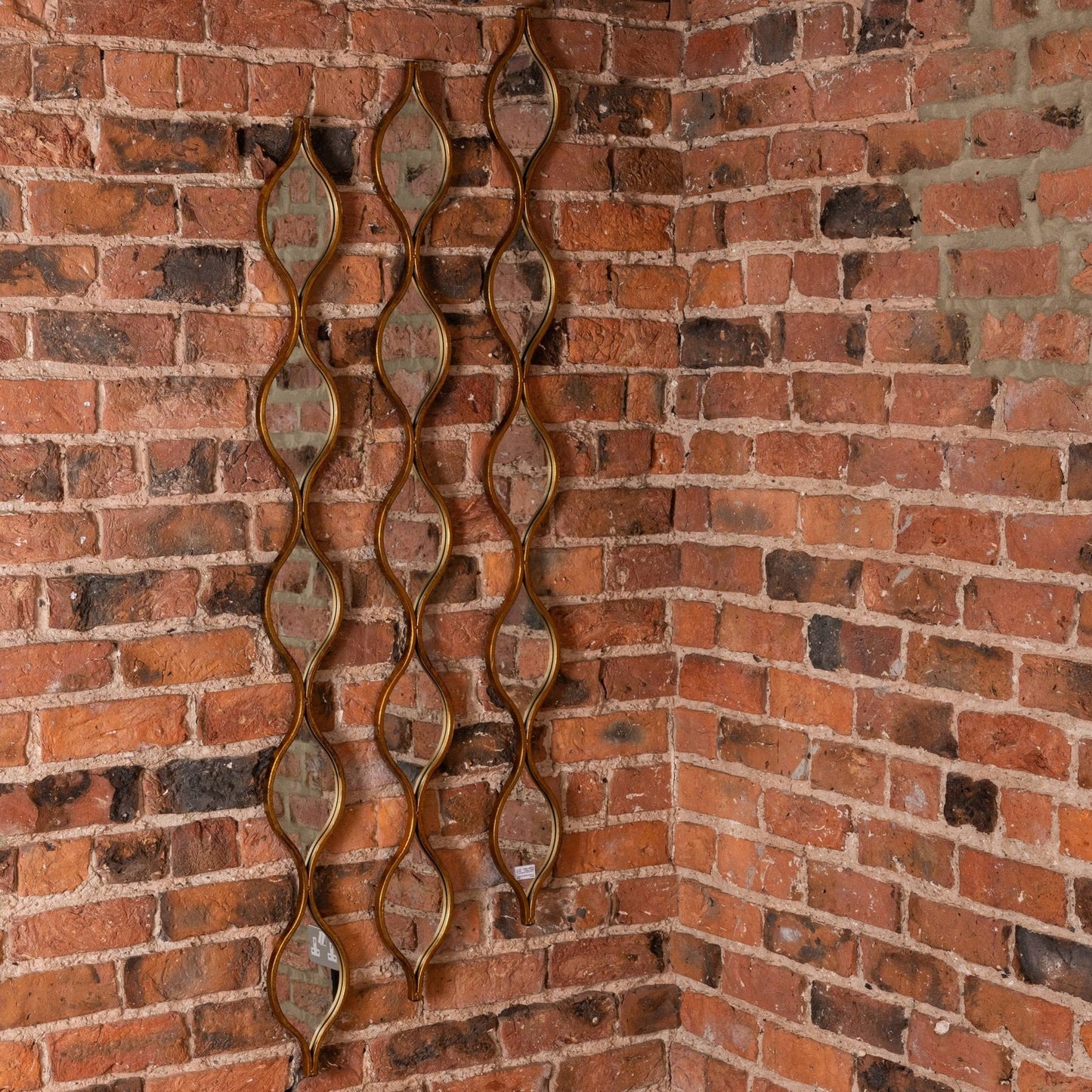 Decorative wall mirror with wavy design on a brick wall