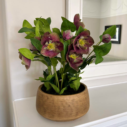 Artificial plant with purple flowers in a wooden pot on a white surface.