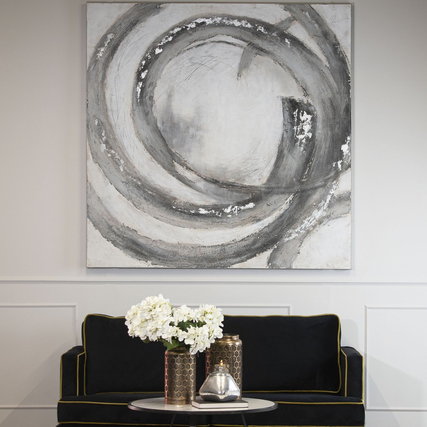 Abstract black and white painting on a wall above a black sofa with decorative items.