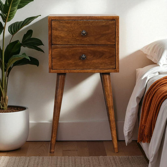 Wooden nightstand with two drawers next to a bed with a plant in the corner.