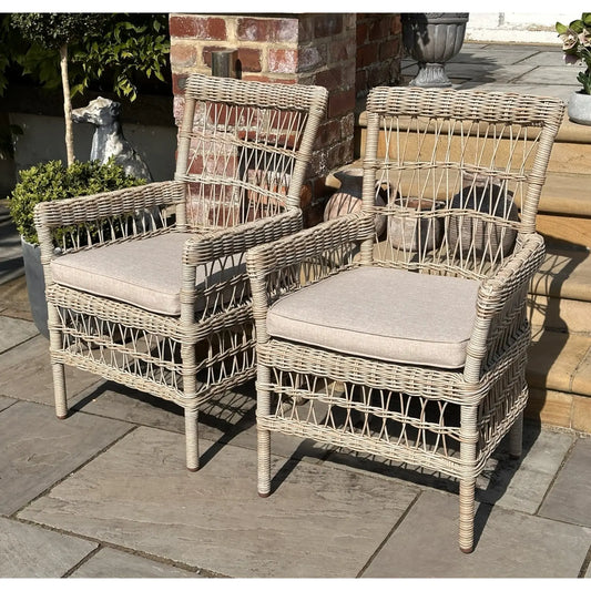 Two wicker chairs with cushions on a stone patio.