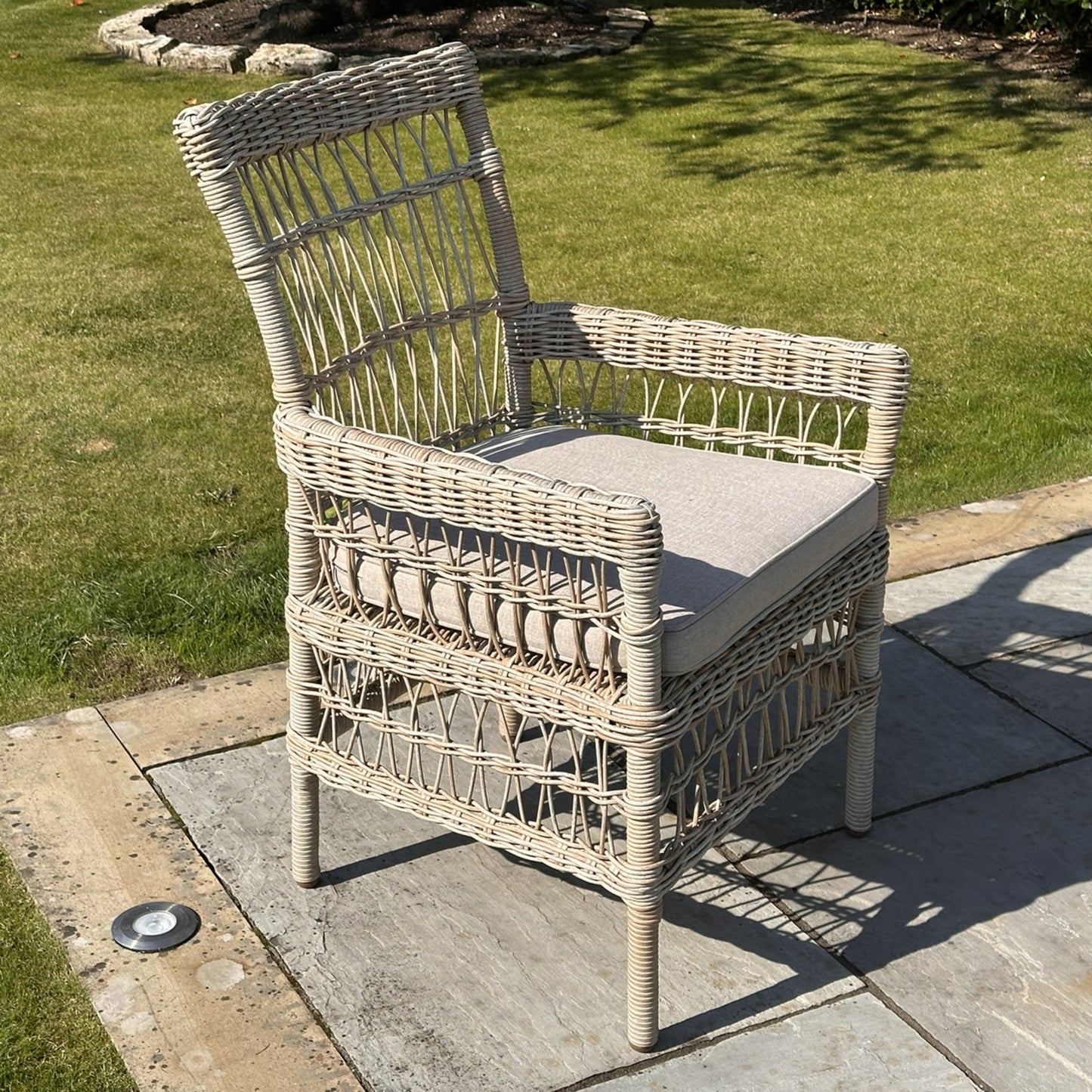 Wicker chair with a cushion on a patio area with grass in the background