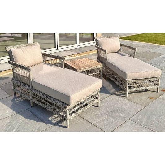 Two wicker outdoor lounge chairs with beige cushions on a stone patio.