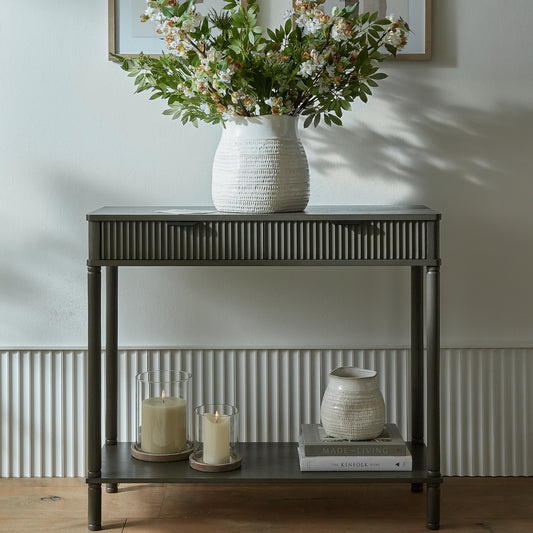 Console table with decorative items including a vase with flowers, candles, and books against a neutral wall.