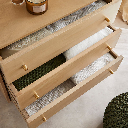 Wooden dresser with open drawers containing folded clothes on a light-colored floor.