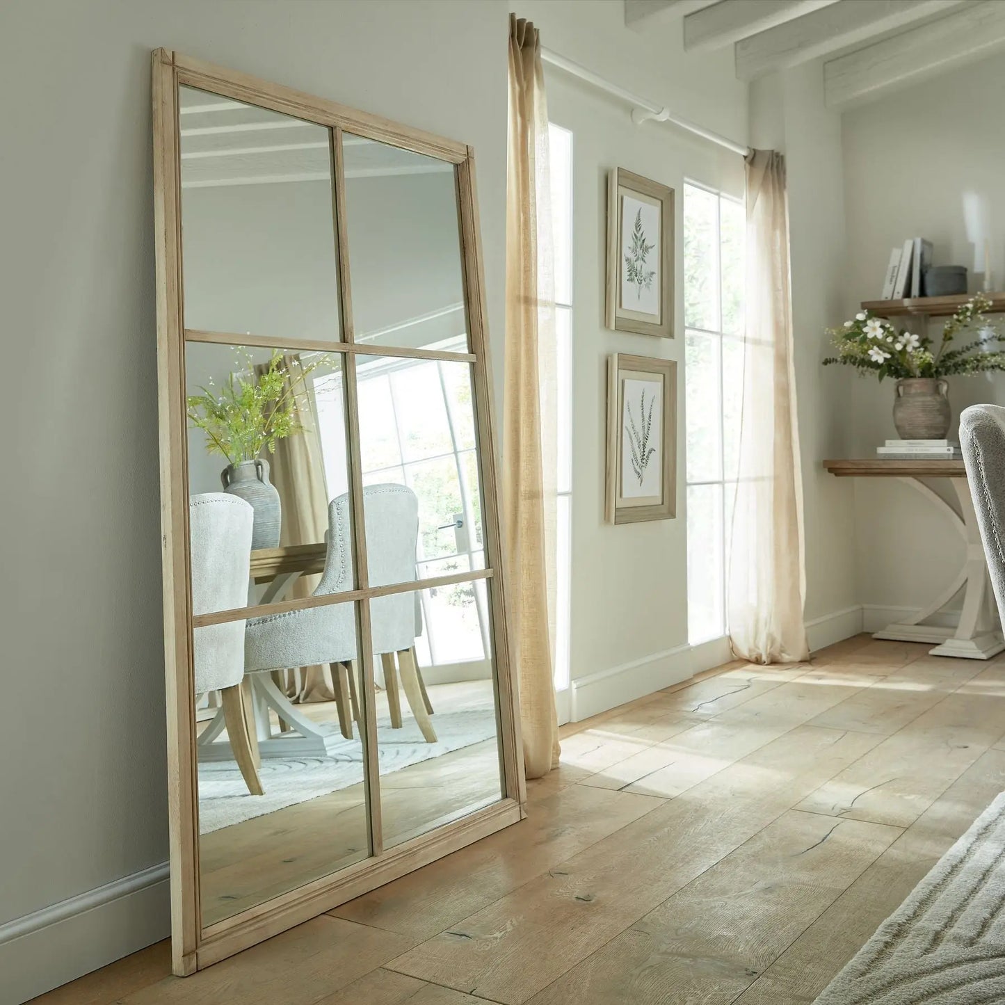 Large floor mirror with wooden frame in a room with light-colored walls and wooden flooring.