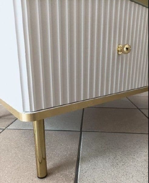 White cabinet with gold legs and handle on a tiled floor