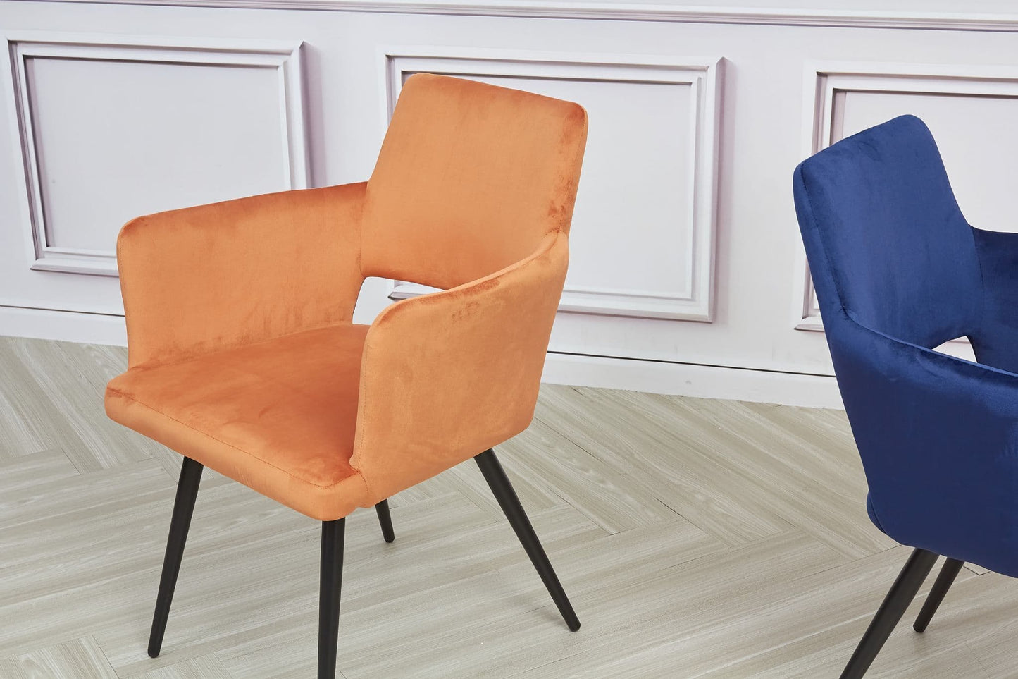 Orange and blue chairs on a light wooden floor with white paneled walls.