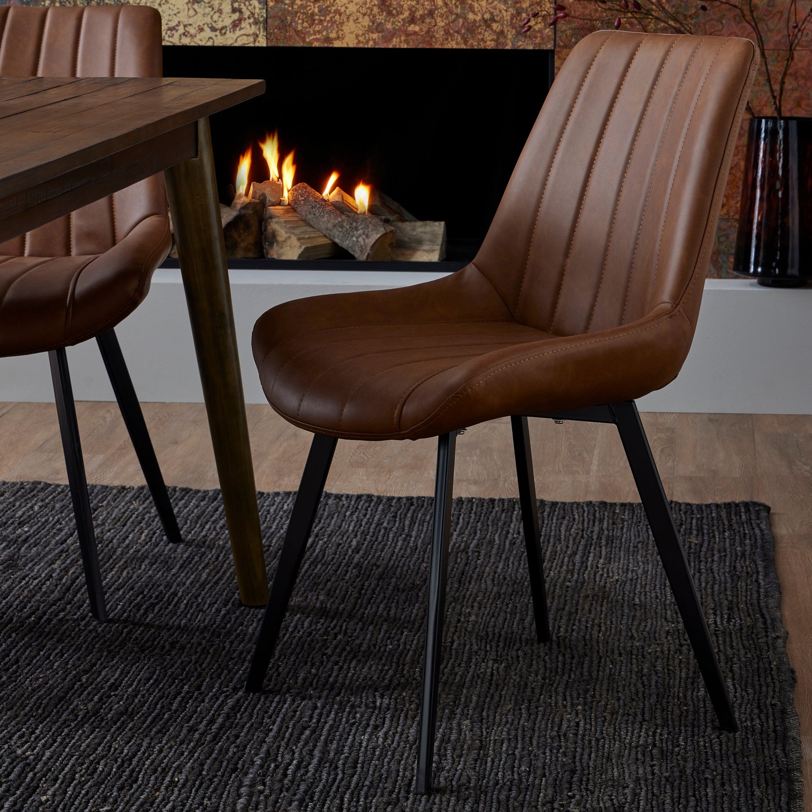 Brown leather chair in front of a fireplace with a wooden table and additional chairs.