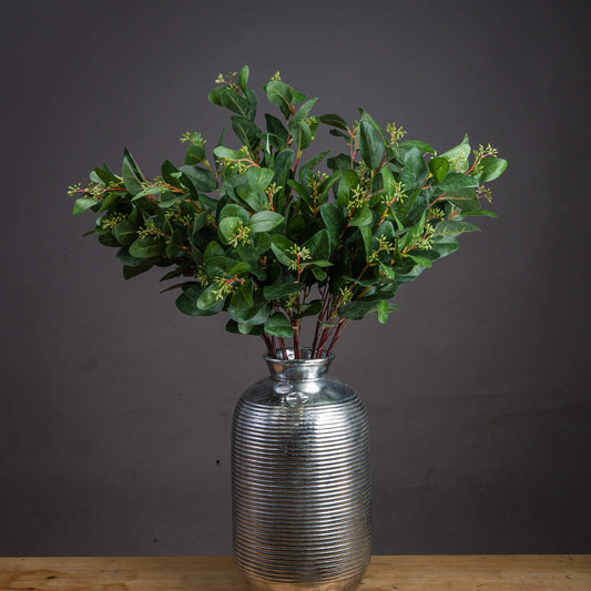 Silver vase with green foliage on a wooden surface against a dark background