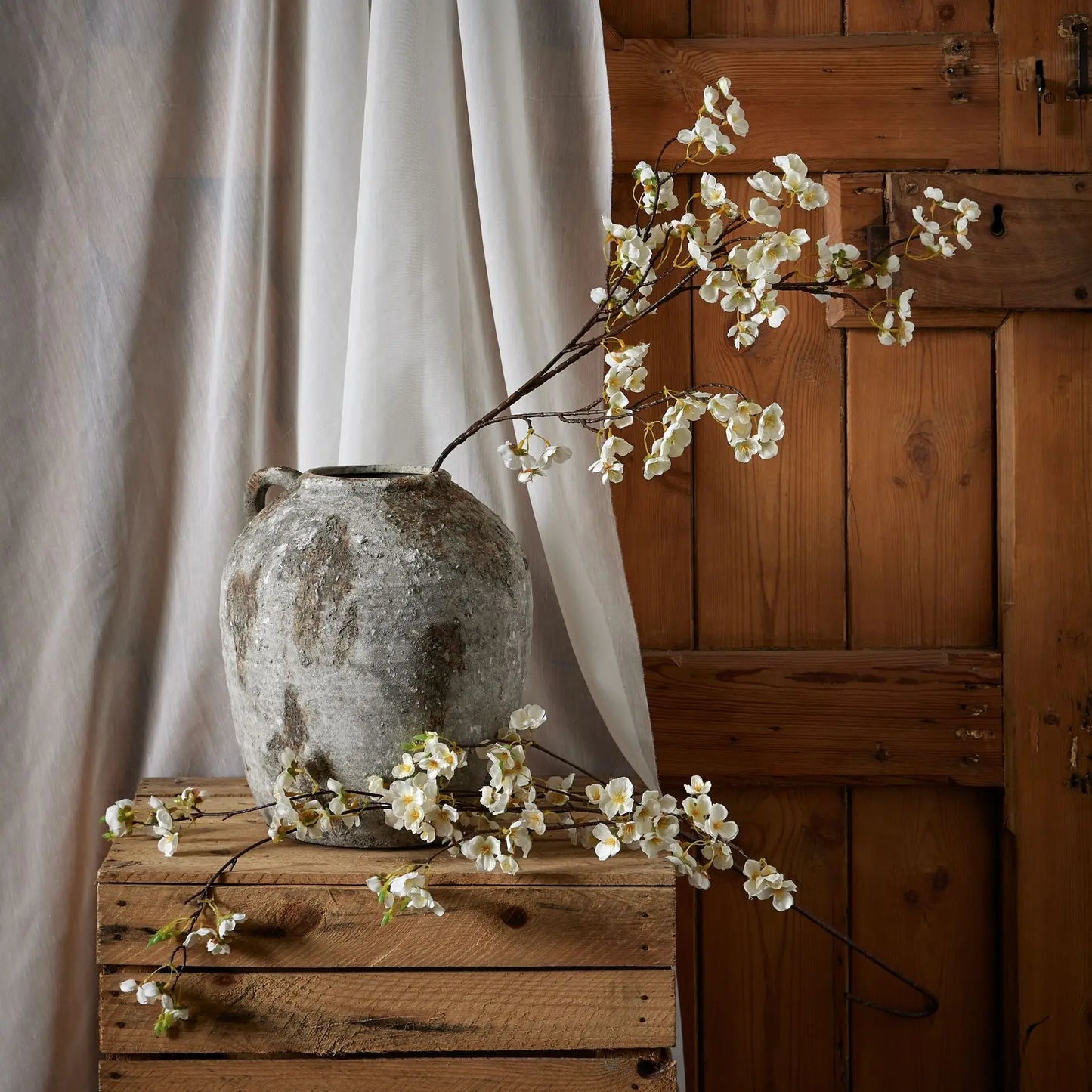 Vintage-style vase with white flowers on a wooden surface against a wooden wall.