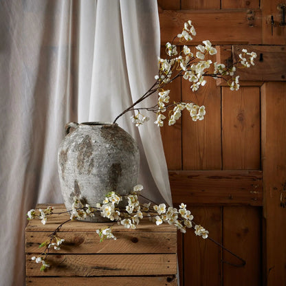 Vintage-style vase with white flowers on a wooden surface against a wooden wall.