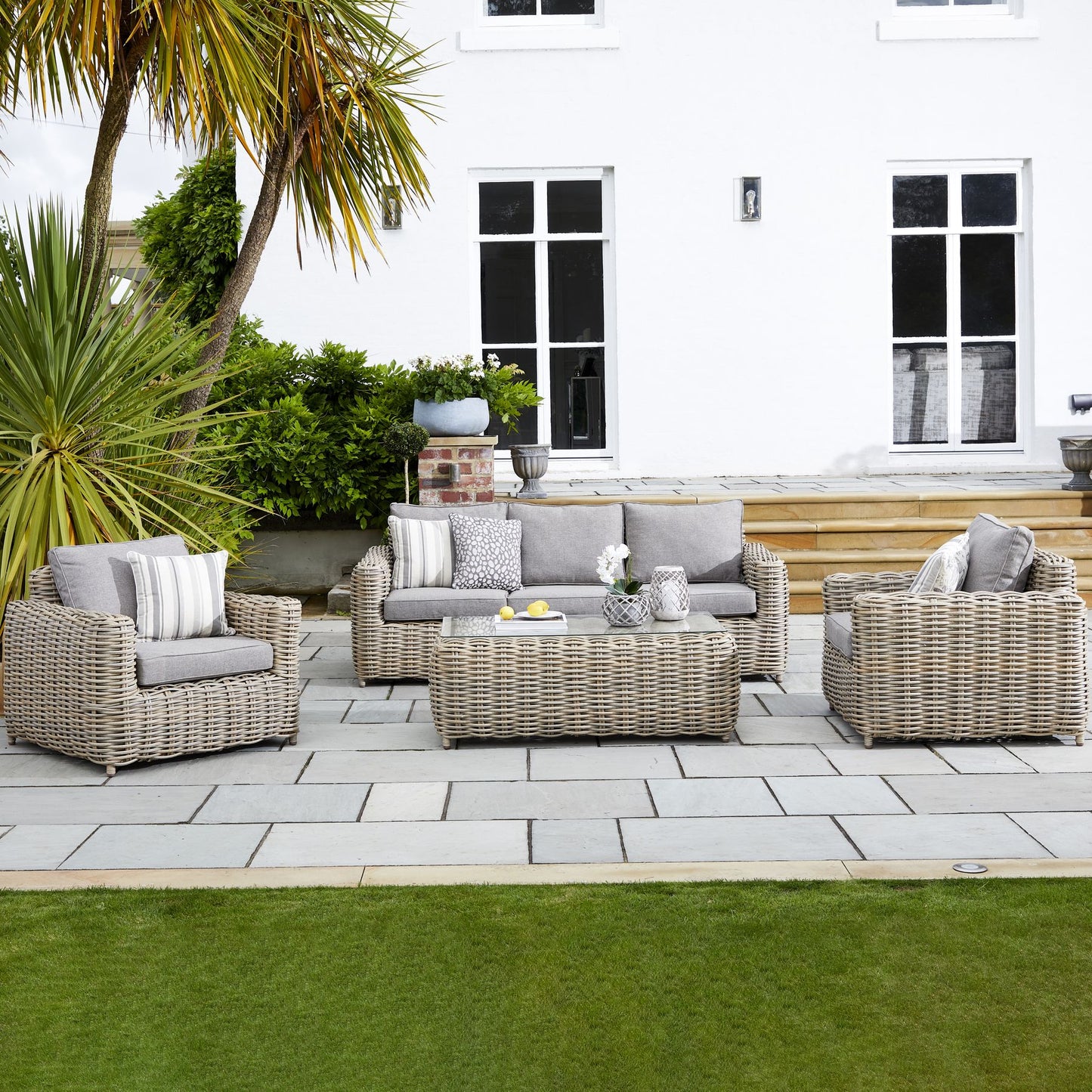 Outdoor patio set with wicker furniture on a stone patio in front of a white house.