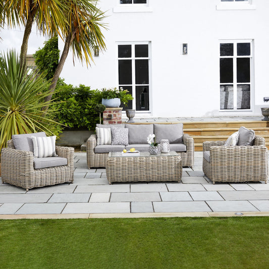 Outdoor patio set with wicker furniture on a stone patio in front of a white house.