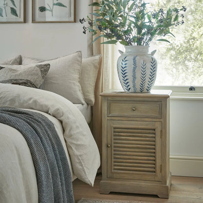 Bedroom with a wooden nightstand, bed with pillows, and vase with plants.