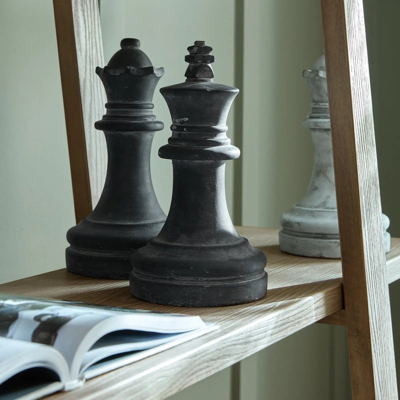 Two large black chess pieces on a wooden shelf with a magazine underneath.