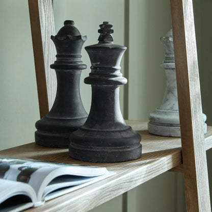 Two large black chess pieces on a wooden shelf with a magazine underneath.