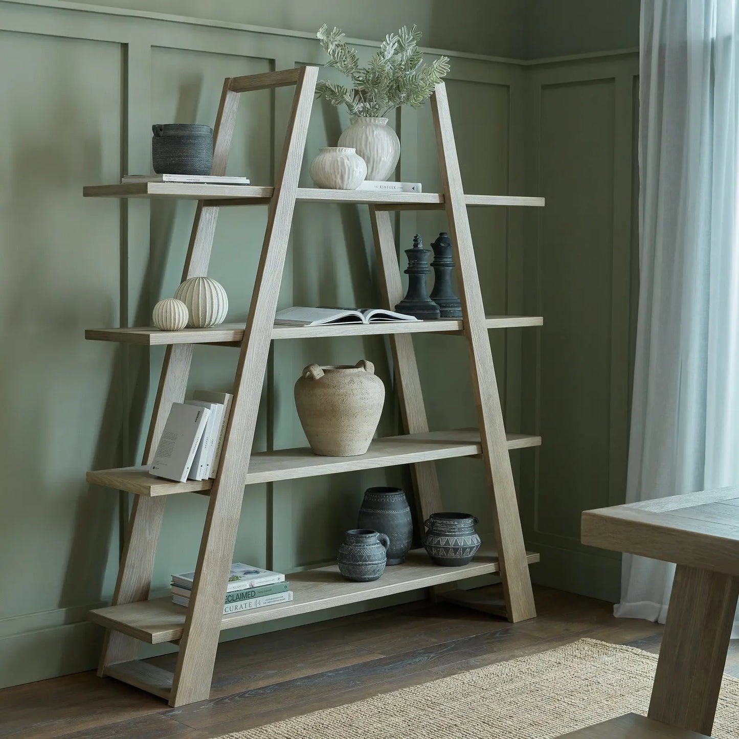 Wooden ladder shelf with decorative items against a green wall