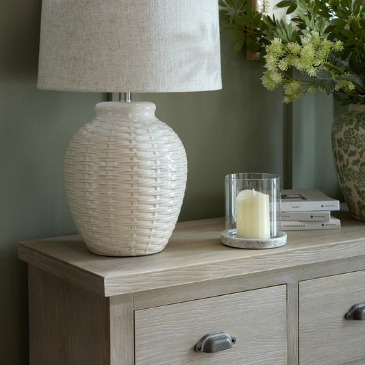 Decorative lamp on a wooden sideboard with a candle and books in the background.
