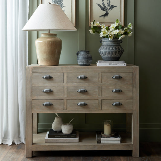 Wooden dresser with decorative items including a lamp, vases, and books against a green wall.
