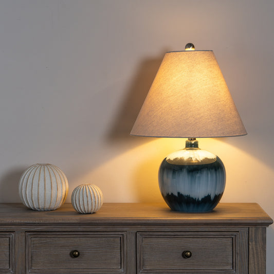 Table lamp with a textured shade on a wooden sideboard next to decorative spheres.