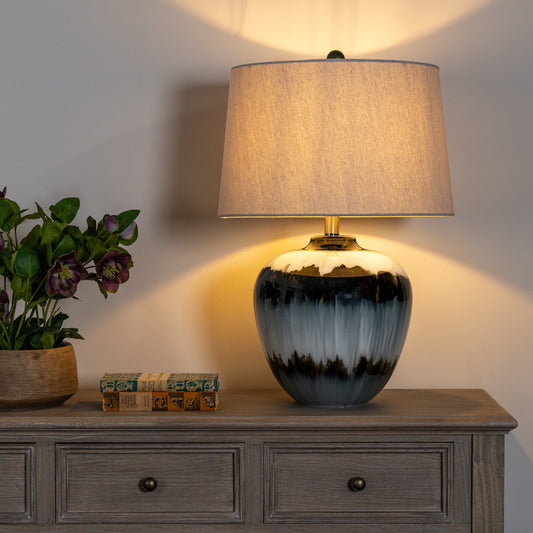 Decorative lamp on a wooden side table with a plant and books in the background.