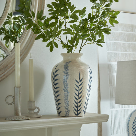 Decorative vase with leaf patterns on a shelf next to candles and a lamp.