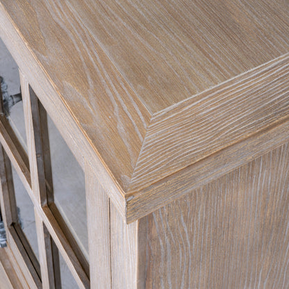Close-up of a light oak wood cabinet corner with a raised apron and glass-paneled door frame.
