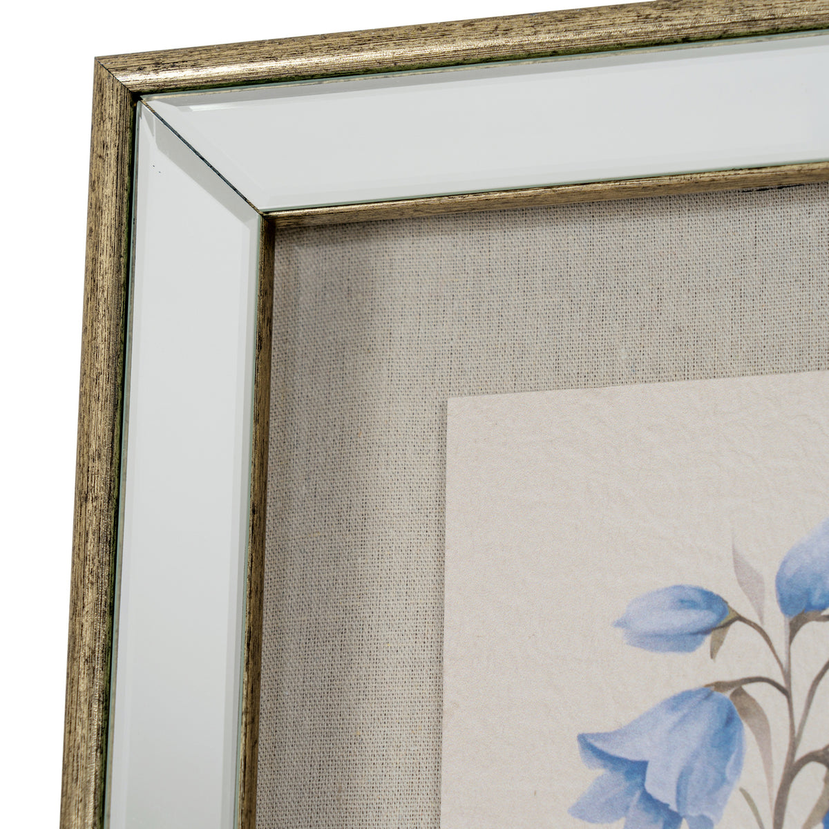 Close-up of a framed wall art piece showing a distressed metallic gold frame, clear glass, textured beige linen backing, and part of a floral print with blue flowers on a white background.