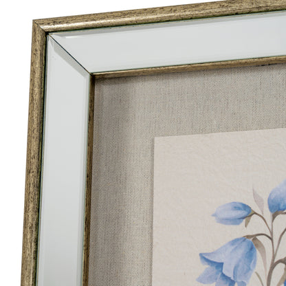 Close-up of a framed wall art piece showing a distressed metallic gold frame, clear glass, textured beige linen backing, and part of a floral print with blue flowers on a white background.
