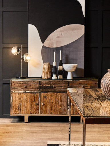 Wooden sideboard with decorative items against a black wall with abstract art.