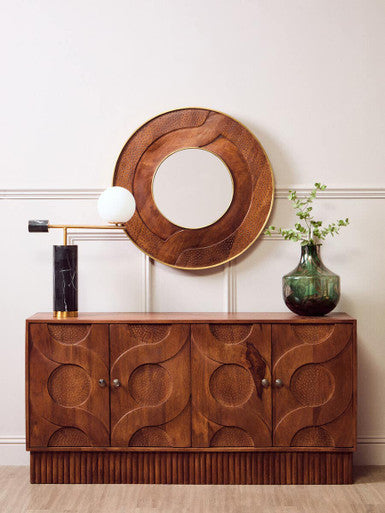 Wooden sideboard with decorative mirror and vases against a white wall