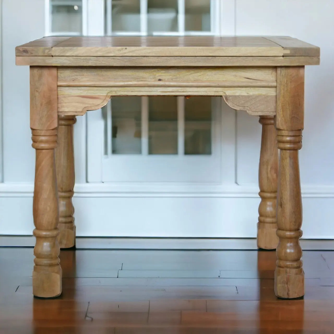 Wooden table with turned legs in a room with white walls and wooden floor.
