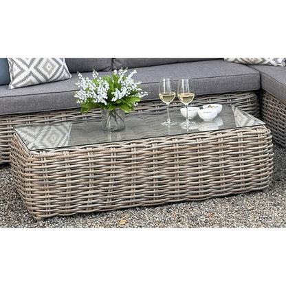 Outdoor patio set with wicker coffee table, cushions, and decorative items on a gravel surface.