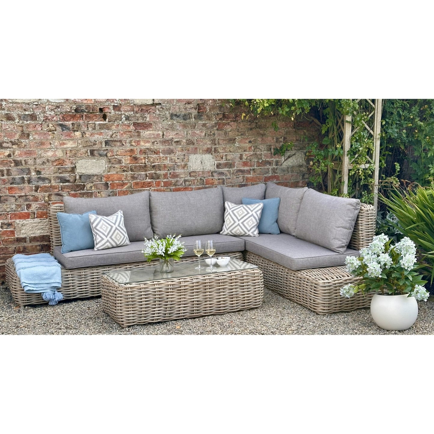 Outdoor patio set with sectional sofa, coffee table, and decorative elements against a brick wall.