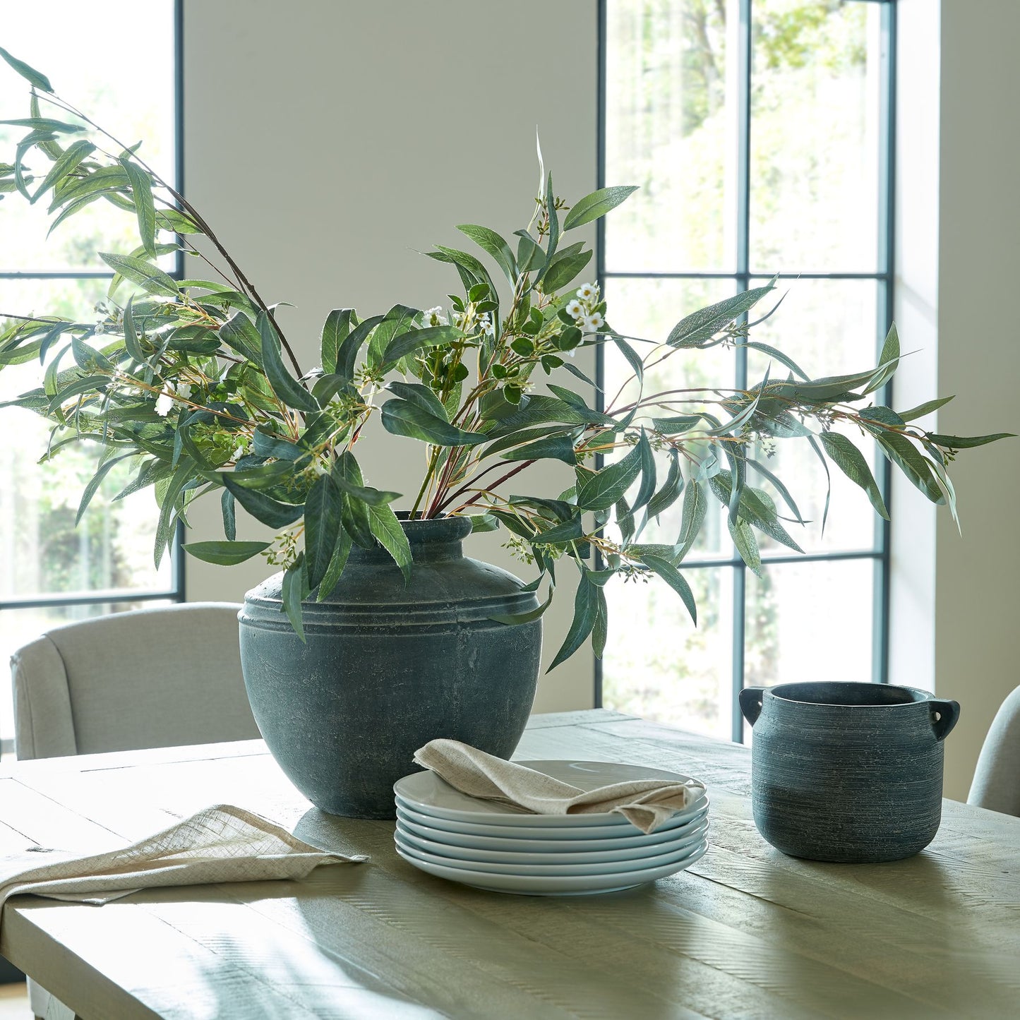 Decorative setting with ceramic pots and greenery on a table in a bright room.