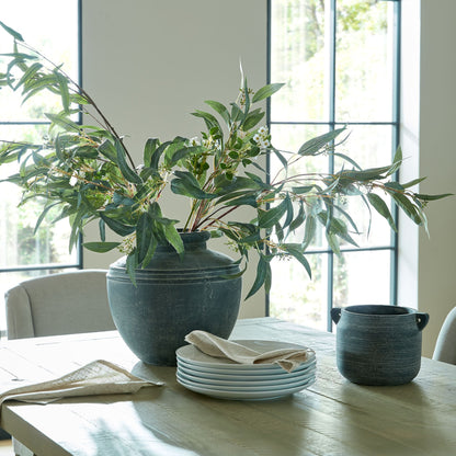 Decorative setting with ceramic pots and greenery on a table in a bright room.
