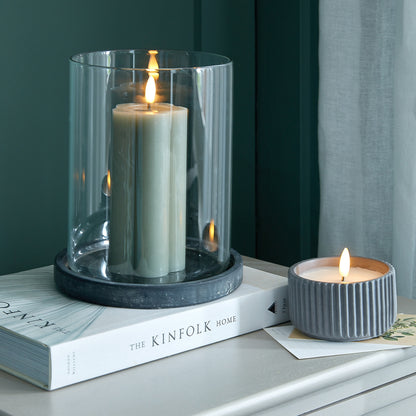Two candles, one in a glass holder and the other in a ribbed container, on a surface with a book titled 'The Kinfolk Home'.