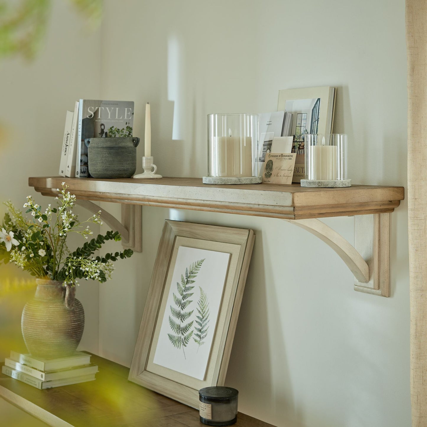 Wooden shelf with decorative items including candles, books, and a framed picture in a home setting.