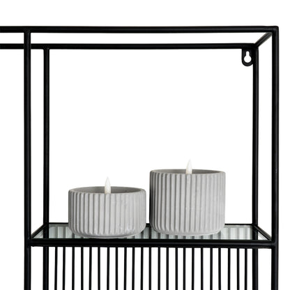 Two gray candles in holders on a black metal shelf with a white background