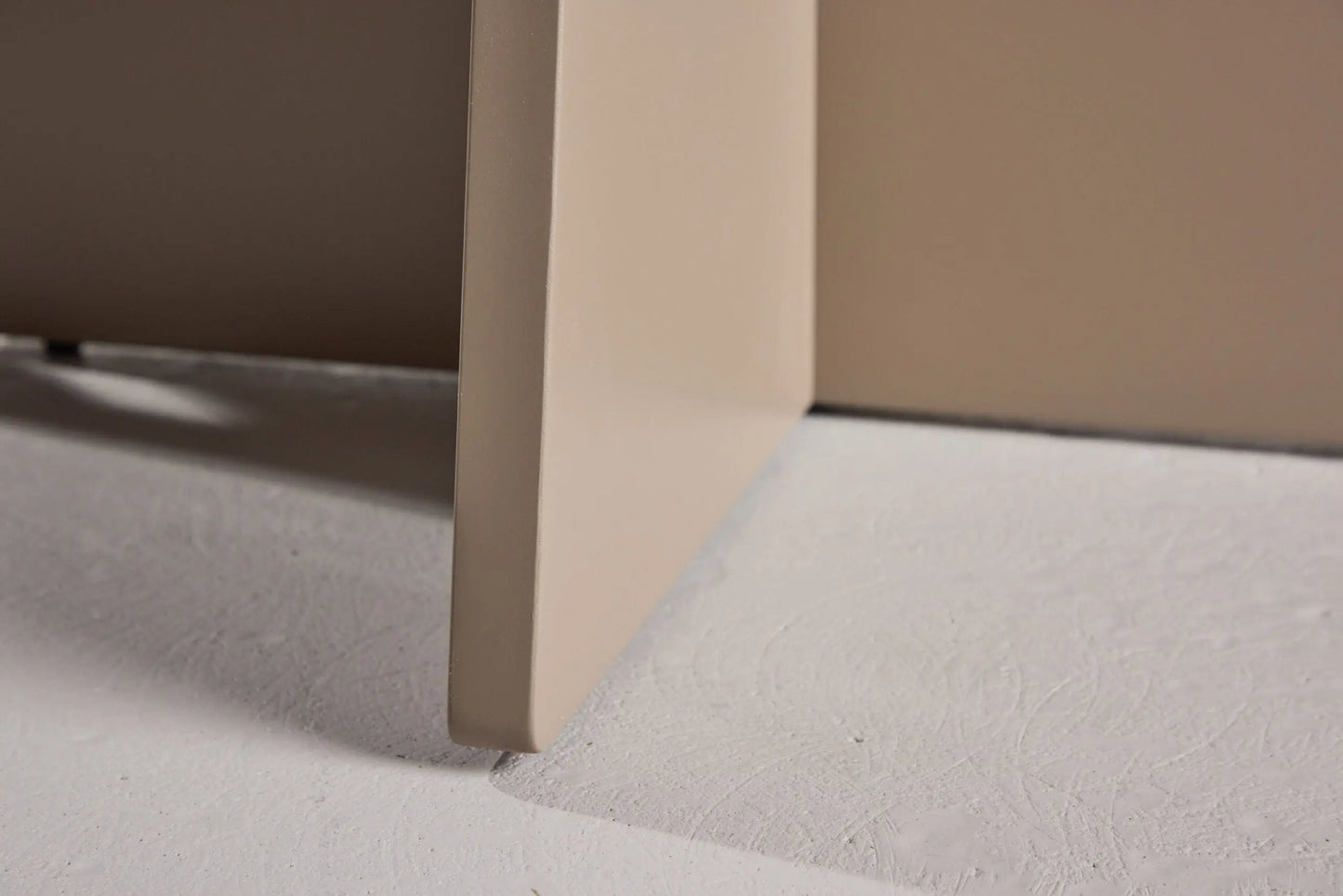 Close-up of a corner of a beige piece of furniture on a light gray floor.