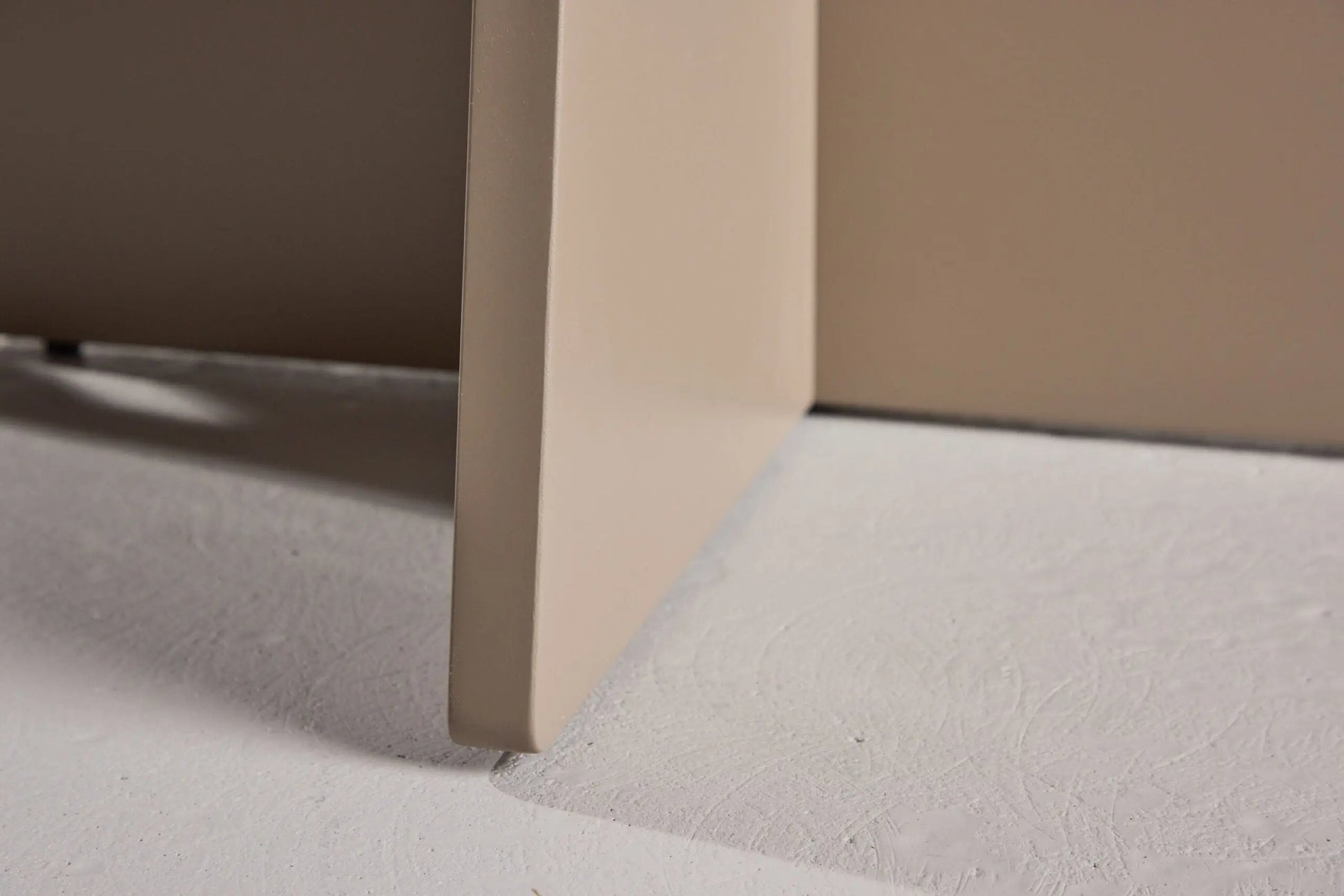 Close-up of a corner of a beige piece of furniture on a light gray floor.