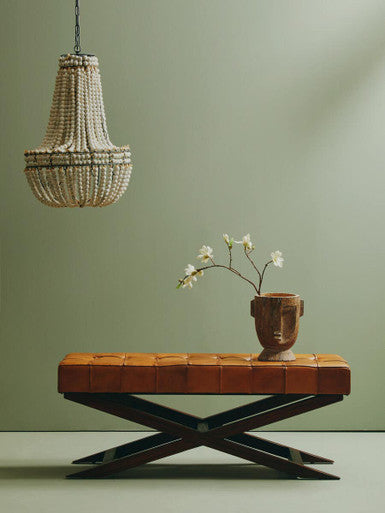 Chandelier hanging above a brown leather bench with a vase of flowers on a green wall.