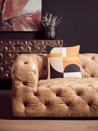 Brown tufted sofa with a decorative pillow in a living room setting.